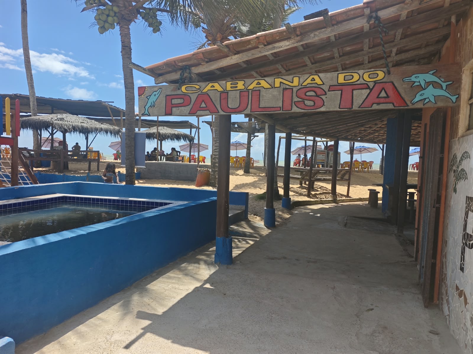 Entrada da Cabana do Paulista com a placa da cabana, piscina e vista para a praia